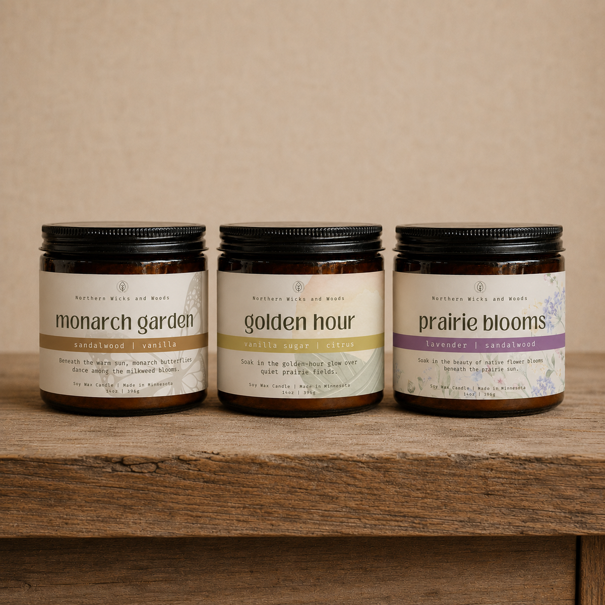 Three amber glass jars of Butter Bells and Woods candles with black lids are lined up on a rustic wooden shelf against a neutral beige background. The labels read 'monarch garden', 'golden hour', and 'prairie blooms'.